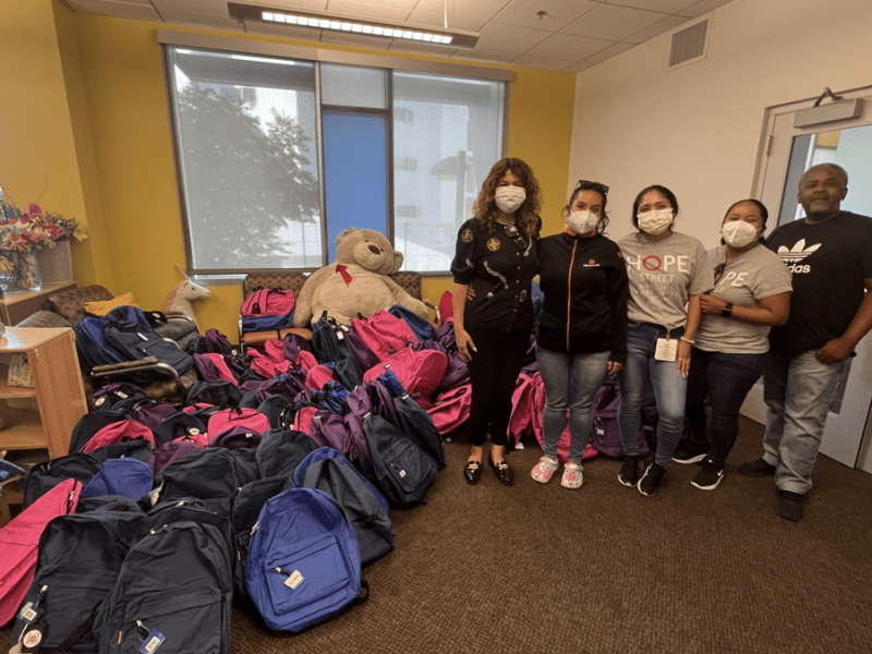 Members of the Hope Street Margolis Family Center, the Assistance League of Los Angeles pose next to the donated backpacks in the facility's library.