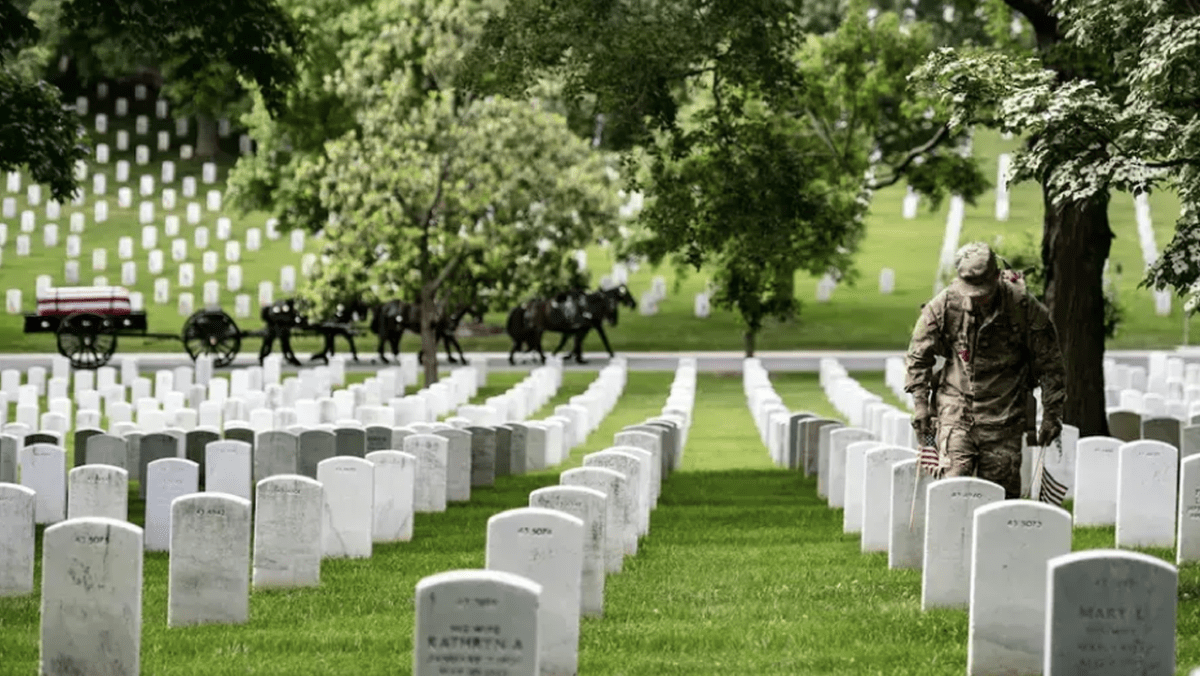 A soldier places a flag at a gravestone in Arlington National Cemetery as part of the annual pre-Memorial Day tradition called Flags In. May 26, 2022.