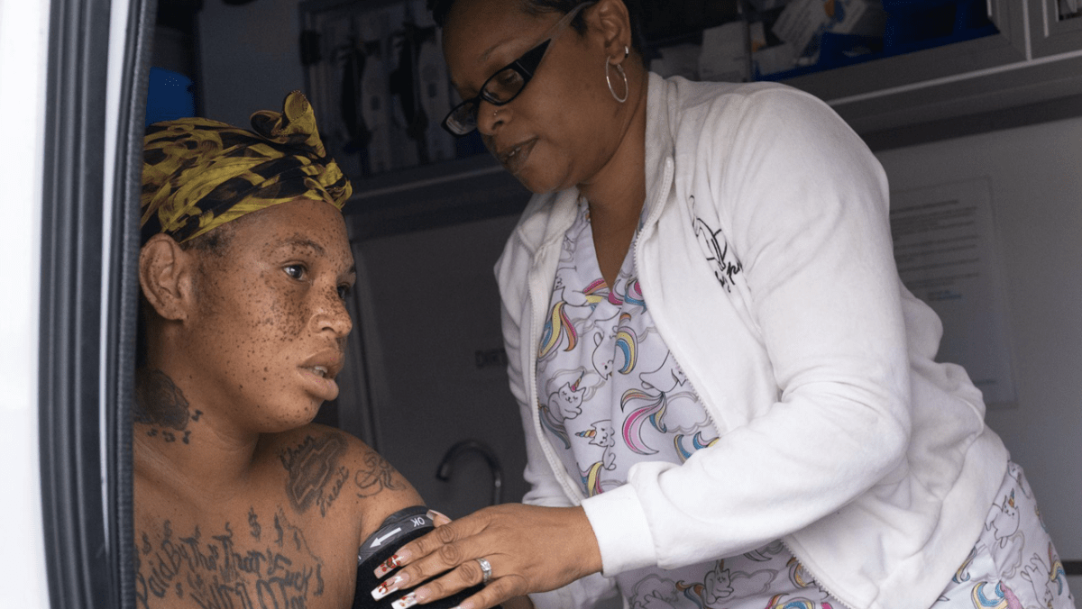 Inside a van that doubles as a mobile clinic, Desteny Benson (right), a clinical support partner at Healthcare in Action, takes the blood pressure of Dominique, a patient in San Bernardino on May 1, 2024. Part of the success of Healthcare in Action is providing services by meeting people where they are. This includes providing onsite lab work and tests, which are typically out of reach for unhoused communities due to lack of access to transportation to clinics, wait times and internet access to receive results.