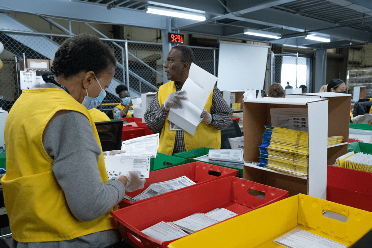 Staff at the San Bernardino Registrar of Voters extract ballots from original envelopes in preparation to scan and organize them by precinct.