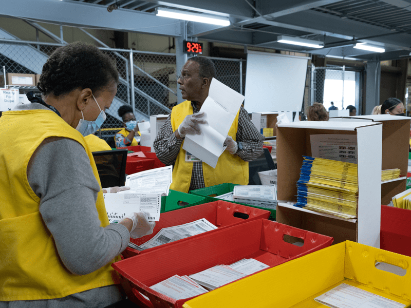 Staff at the San Bernardino Registrar of Voters extract ballots from original envelopes in preparation to scan and organize them by precinct.